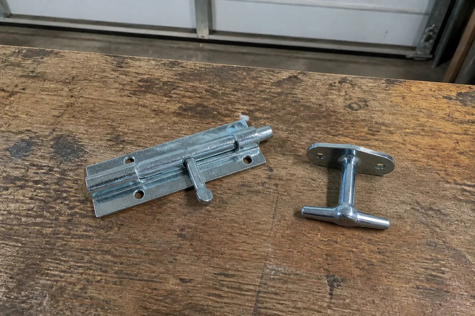Detached slide bolt and T-handle on a wooden garage workbench. — Garage Door Manual Lock Repair, Kawartha Lakes