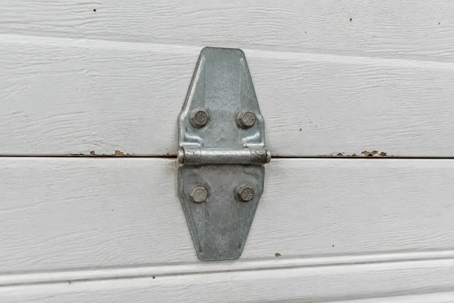 Metal center hinge across a seam in a white sectional garage door. — Garage Door Hinge Replacement, Kawartha Lakes